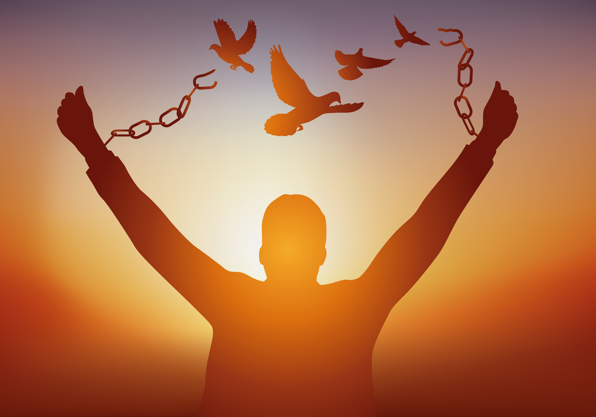 A man frees himself by breaking his chains while watching doves fly away.