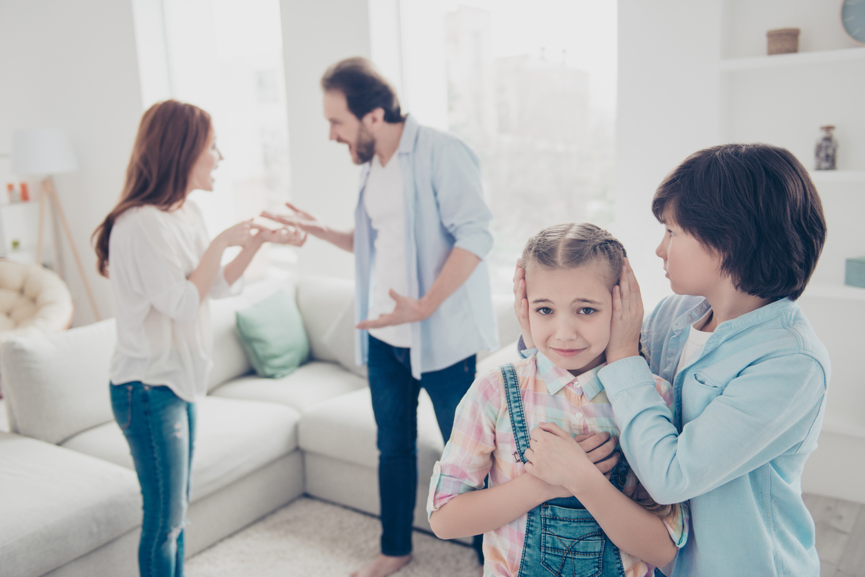 Portrait of nervous annoyed daddy and mom screaming at each other gesturing with hands on blurred background, older brother closing ears of upset misery sister. Crisis disagreement concept